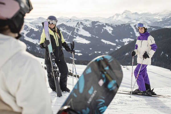 Two single skiers chatting to a snowboarder